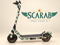 Segway Ninebot E3 mit SCARAB Skin: geflügelte Skarabäen in Petrol und Türkis mit ockerfarbenen Details auf Elfenbein. Designvisualisierung; originale graue Trittmatte bleibt erhalten.